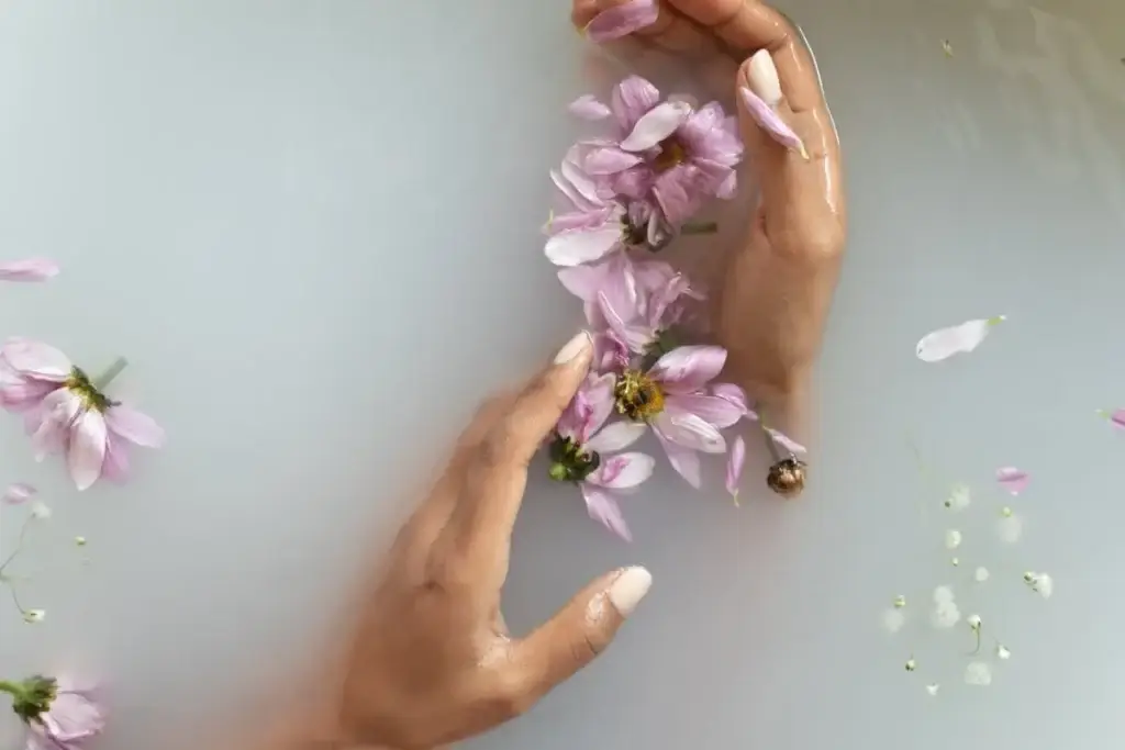 Hands gently holding pink flowers in soft water representing calming, natural skincare and relaxation